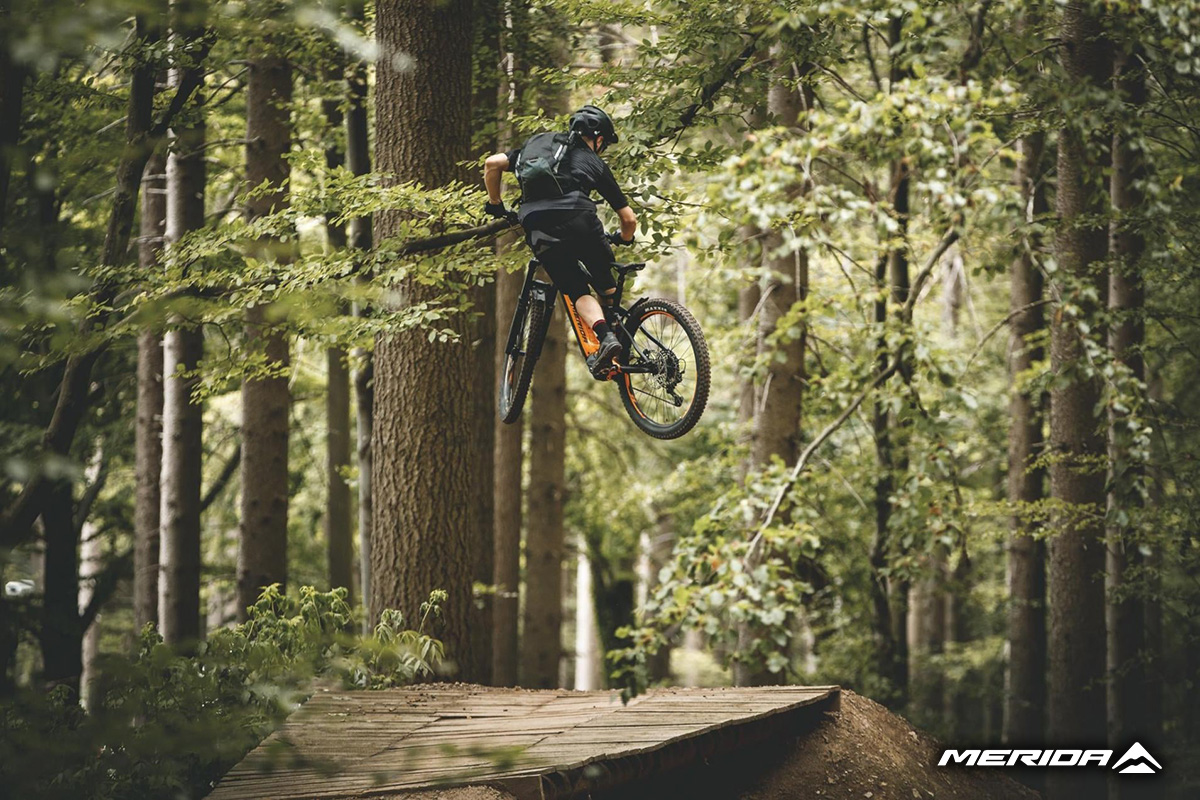 Un uomo salta su una rampa nel bosco con una delle nuove mountainbike Merida 2021